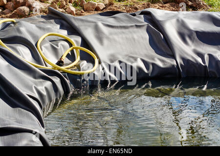 Nuovo stagno con rivestimento in gomma è riempita con acqua per la prima volta. Foto Stock