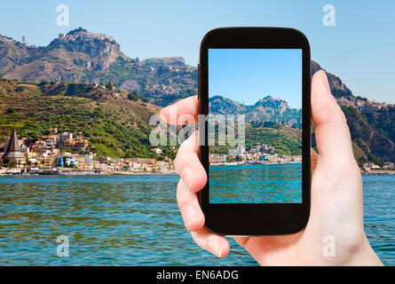 Concetto di viaggio - tourist prende foto di Taormina - popolare località turistica sulla montagna e Gardini Naxos Beach, SICILIA su smart Foto Stock