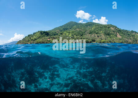 Un over in vista della barriera corallina al di sotto della superficie dell'oceano e dell'isola di Vulcano Pura nello stretto di Pantar, Alor, Indonesia Foto Stock