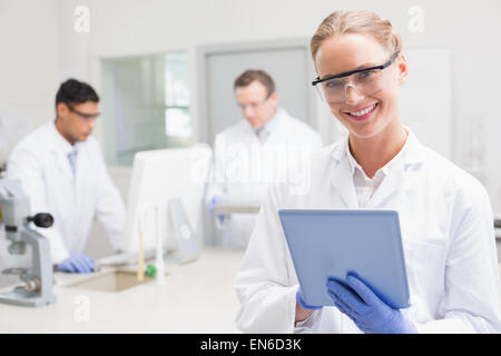 Scienziato sorridente utilizzando tablet mentre i colleghi lavorando dietro Foto Stock