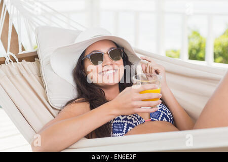 Bella bruna relax su una amaca e bere il succo d'arancia Foto Stock