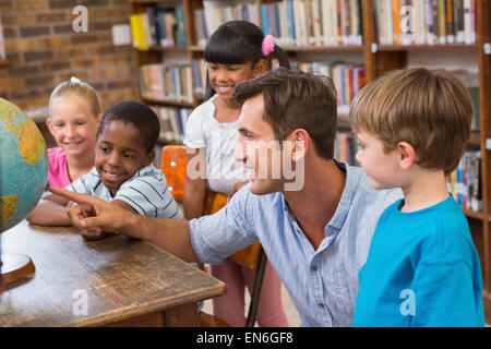 Carino gli alunni e gli insegnanti guardando il globo in biblioteca Foto Stock