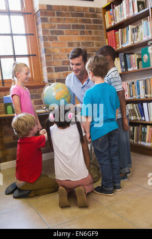 Carino gli alunni e gli insegnanti guardando il globo in biblioteca Foto Stock