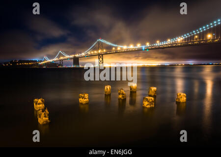 Pier palificazioni e il San Francisco - Oakland Bay Bridge di notte, a San Francisco, California. Foto Stock