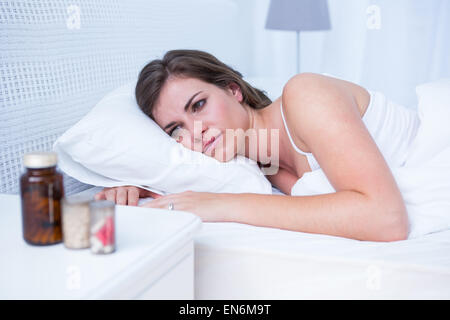 Donna triste guardando pillole nel letto Foto Stock