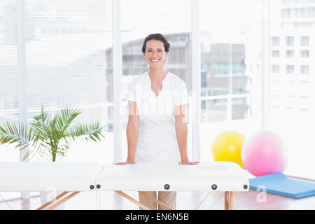 Medico sorridente guardando la telecamera dietro di lettino da massaggio Foto Stock