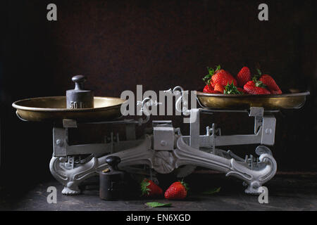 Pesi e scale vintage con fragole fresche su sfondo scuro Foto Stock