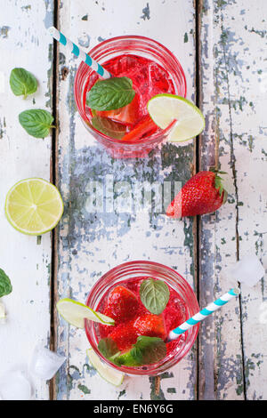 Due bicchieri con cocktail retrò tubi e caraffa di vetro di fragole fatta in casa la limonata, servita con fragole fresche, menta, calce Foto Stock