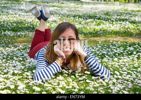 Bruna ragazza distesa in erba pieno di fiori Foto Stock