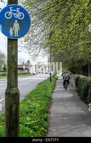 Vista posteriore di un ciclista maschio su una condivisa sentiero pedonale e cyclepath con segno blu in primo piano su una strada principale. Foto Stock
