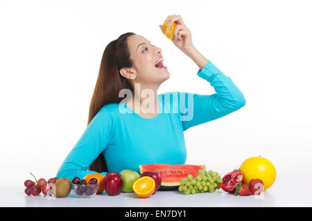 Donna spremendo il succo di arancia nella sua bocca Foto Stock