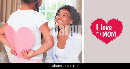 Immagine composita della bella madre seduta sul divano con la figlia per nascondere la scheda di cuore Foto Stock