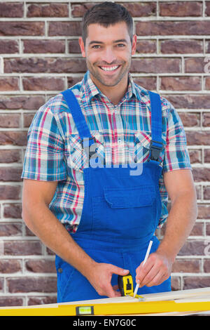 Immagine composita di fiduciosa carpenter marcatura sul listone con nastro di misurazione Foto Stock