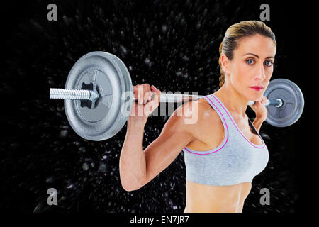 Immagine composita della femmina forte sollevamento crossfitter barbell dietro la testa guardando la fotocamera Foto Stock