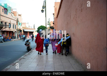 Famiglia di ritorno da scuola a scuola correre lungo una strada principale in marrakech Africa del nord Foto Stock