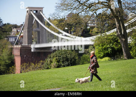 Una donna che cammina il suo cane passato il ponte sospeso di Clifton in un assolato pomeriggio di primavera. Foto Stock
