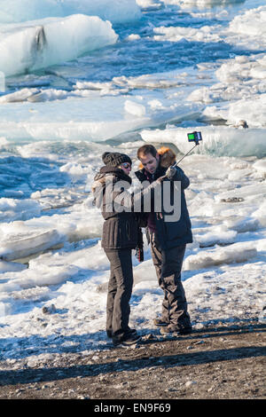 Coppia di turisti che prendono selfie con selfie bastone a Jokulsarlon Glacial Lagoon, sul bordo del Parco Nazionale Vatnajokull, Islanda nel mese di febbraio Foto Stock