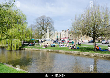 Gli ospiti godono di pic-nic a lato del Fiume Windrush in esecuzione attraverso Bourton sull'acqua in Cotswolds Foto Stock