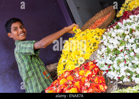 Un ragazzo sorridente prepara un display di fiori e ghirlande a un mercato in stallo Nandyal Foto Stock