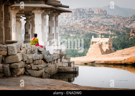 Una donna seduta in alcune fra le antiche rovine di Hampi. Foto Stock