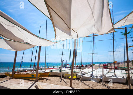Tende da sole in vele forma che copre la zona relax vicino a barche a vela sulla spiaggia di sabbia nella città di Calafell, Costa del Mare Mediterraneo, Catal Foto Stock