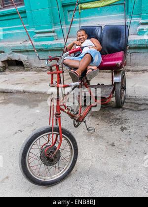 Un ispanico pilota pedicab si stende sul sedile del suo pedicab e sorrisi come egli sia rivolta in avanti nella Habana Vieja, Cuba. Foto Stock