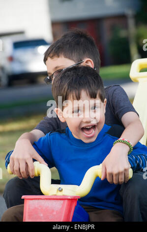 Due fratelli, età di sette e quattro ride una grande ruota tre wheeler nel loro passo carraio. Foto Stock