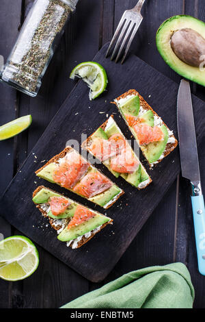 Sandwich con avocado e salmone affumicato su un nero pannello di legno Foto Stock