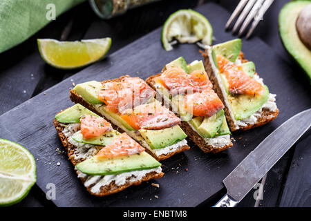 Sandwich con avocado e salmone affumicato su un nero pannello di legno Foto Stock