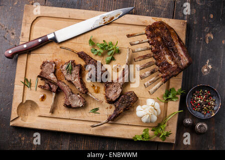 Agnello arrosto nervature e coltello da cucina sul tagliere di legno su sfondo scuro Foto Stock