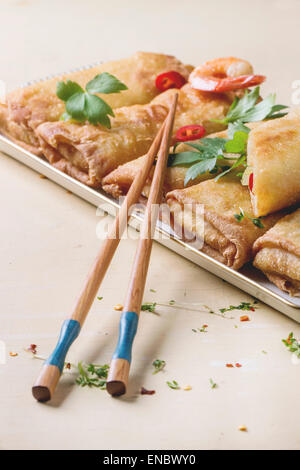 Fritti involtini primavera con verdure e gamberi, serviti con salsa piccante e bastoncini su bianco sullo sfondo di legno. Foto Stock