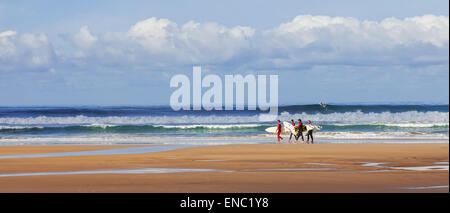 Gruppo di amici surfisti in Costa de Caparica beach. Pioneer iconico punto surf in Portogallo e camminando per trasportare le tavole da surf felice con la tavola da surf onde del mare Foto Stock