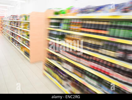 Lunghi scaffali con bottiglie di bevande in grande negozio di generi alimentari negozio di alimentari in un supermercato. Si filtra stock foto sfocate in movimento. Foto Stock