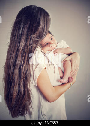 Dolce madre con bambino più piccolo isolato su sfondo grigio, donna con scuri capelli lunghi tenendo la sua preziosa figlia del neonato Foto Stock