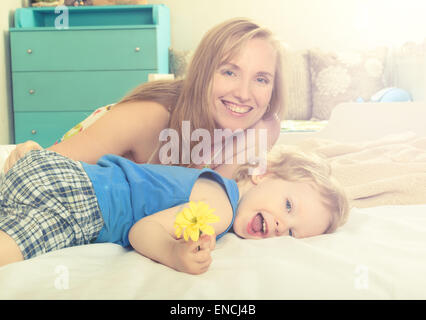 Sorridente abbracciando la mamma con il suo bambino giacente a letto Foto Stock