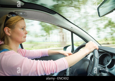 Ritratto di profilo di gravi calma donna attenta e guida sicura auto sulla strada di campagna. Foto Stock
