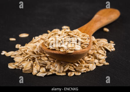 Fiocchi di avena su un cucchiaio di legno sul bordo scuro Foto Stock