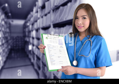 Medico donna in uniforme blu holding medical record nella mani di fronte a sfondo blu del record medico archivi. Foto Stock