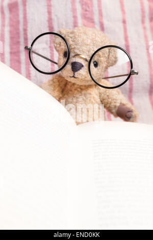 Orsacchiotto di peluche con enormi occhiali vintage la lettura di un libro di fronte a strisce rosa sullo sfondo (copia spazio) Foto Stock