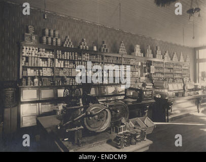 Questa immagine mostra l'interno di un negozio da una data sconosciuta. La scena cattura il design e la disposizione del negozio, compresi scaffali, merci e l'atmosfera generale dello spazio. L'aspetto vintage suggerisce che sia stato preso durante un periodo precedente nella storia della vendita al dettaglio. Foto Stock