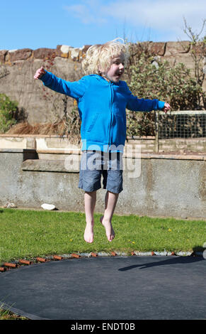 Little Boy saltando su un trampolino in giardino Foto Stock