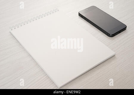 Blocco note con il telefono su un tavolo luminoso Foto Stock