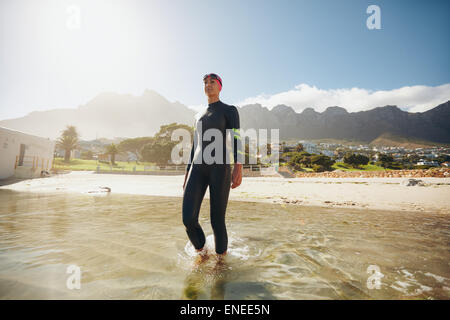 Immagine di montare il giovane triatleta femmina a piedi in mare indossando muta. Triatleta in formazione presso la spiaggia. Foto Stock