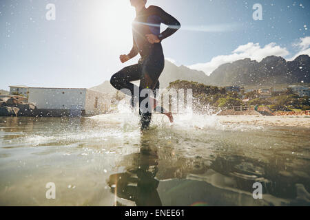 Basso angolo vista del giovane atleta che corre in acqua. I partecipanti eseguono in acqua per l'inizio di una gara di triathlon. Foto Stock