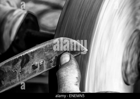 Affilare la lama di un coltello su di una pietra arenaria umido mola Foto Stock