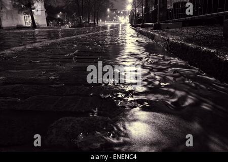 Pioggia di flusso di acqua su una strada acciottolata a Helsinki in Finlandia in autunno piovoso la notte. Foto Stock