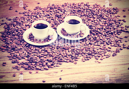 Retro Vintage filtrata foto di due tazze da caffè tra i chicchi di caffè su di un tavolo di legno. Foto Stock