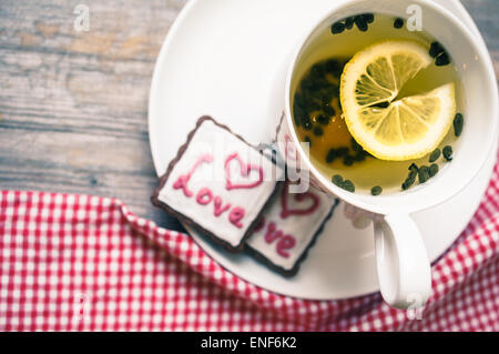 Tazza di tè con limone e i cookie su sfondo di legno. Immagine dai toni Foto Stock