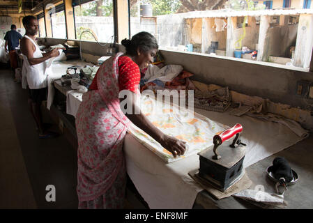 Un impiegato che usa un vecchio ferro riscaldato con carbone che brucia ad un grande bucato a Cochin Fort in Kochi, Kerala, India. Foto Stock