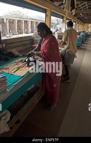 Un impiegato che usa un vecchio ferro riscaldato con carbone che brucia ad un grande bucato a Cochin Fort in Kochi, Kerala, India. Foto Stock